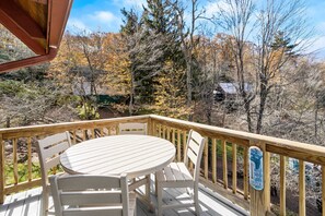 A wooden deck with a round table and white chairs, overlooking a forested area with autumn foliage. - Cozy Mountain Home Near Ski Slopes (Blowing Rock)