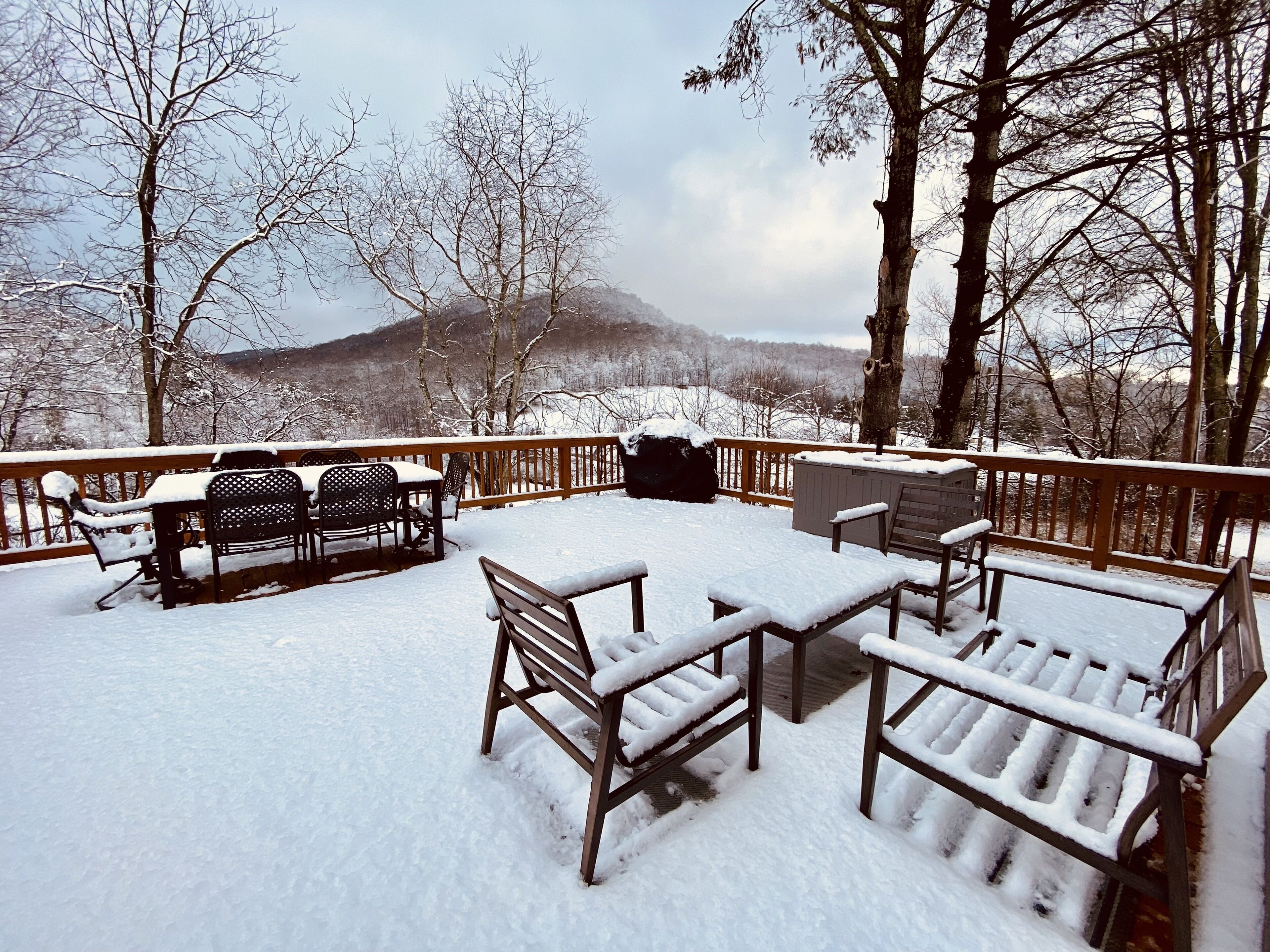 A snow-covered deck with outdoor furniture and a view of a mountain.