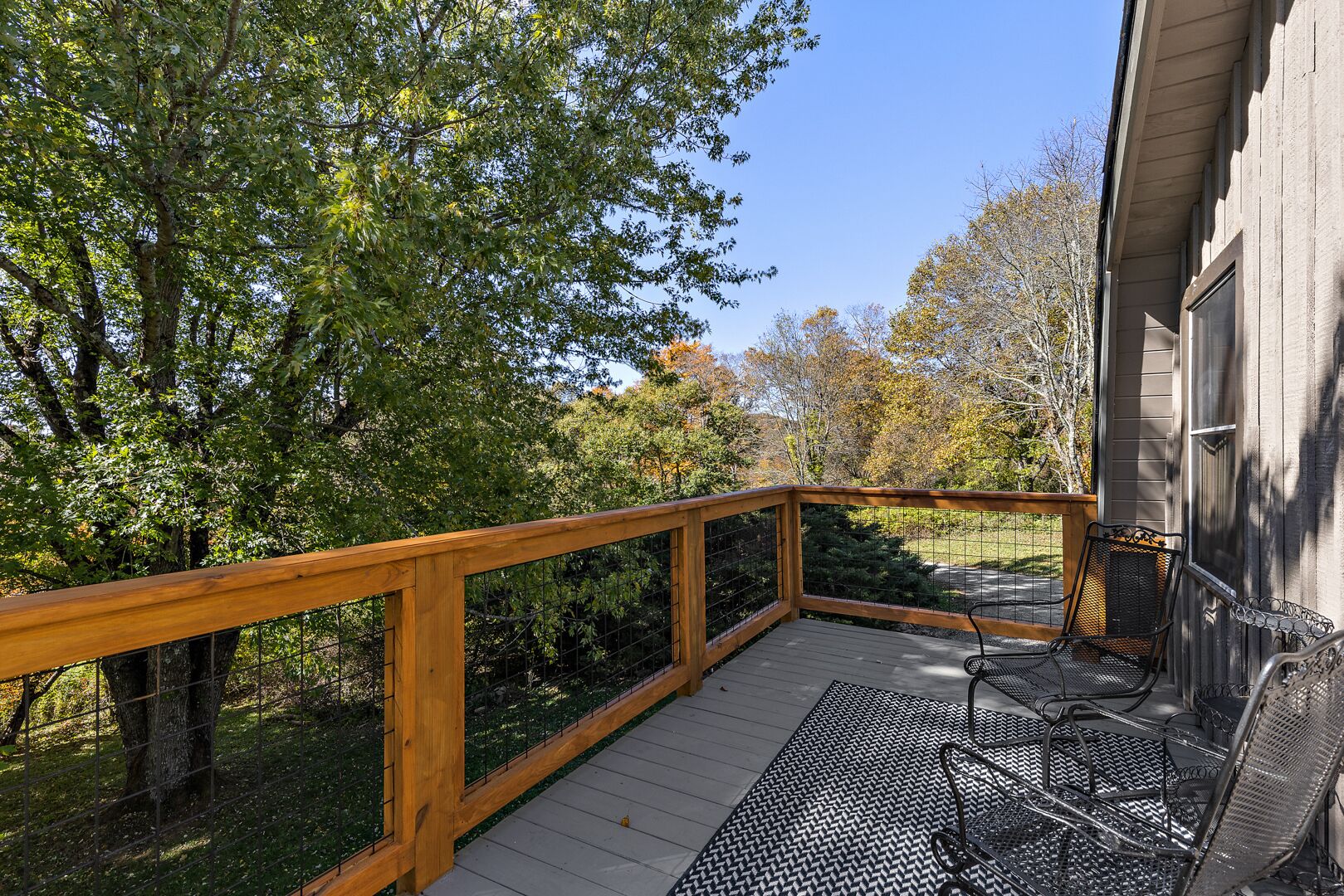 A wooden deck with a railing, surrounded by trees and a house.
