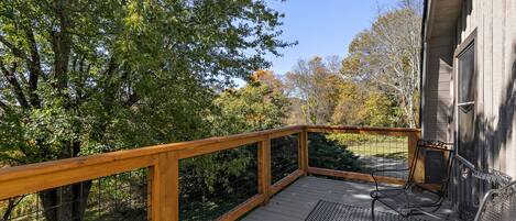 A wooden deck with a railing, surrounded by trees and a house.