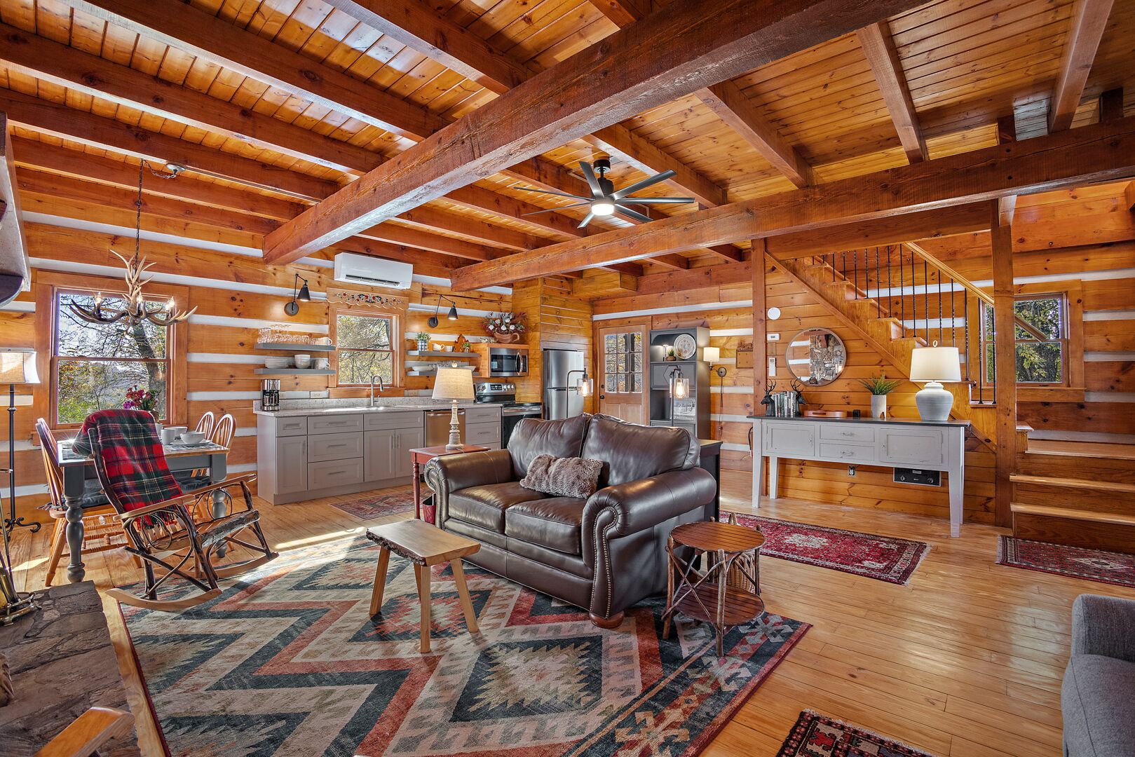 Un intérieur spacieux de chalet en bois, comprenant un coin repas, un canapé en cuir et un escalier.