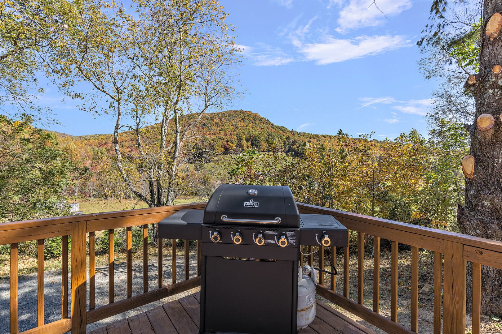 A barbecue grill on a wooden deck with a view of a forested hillside.