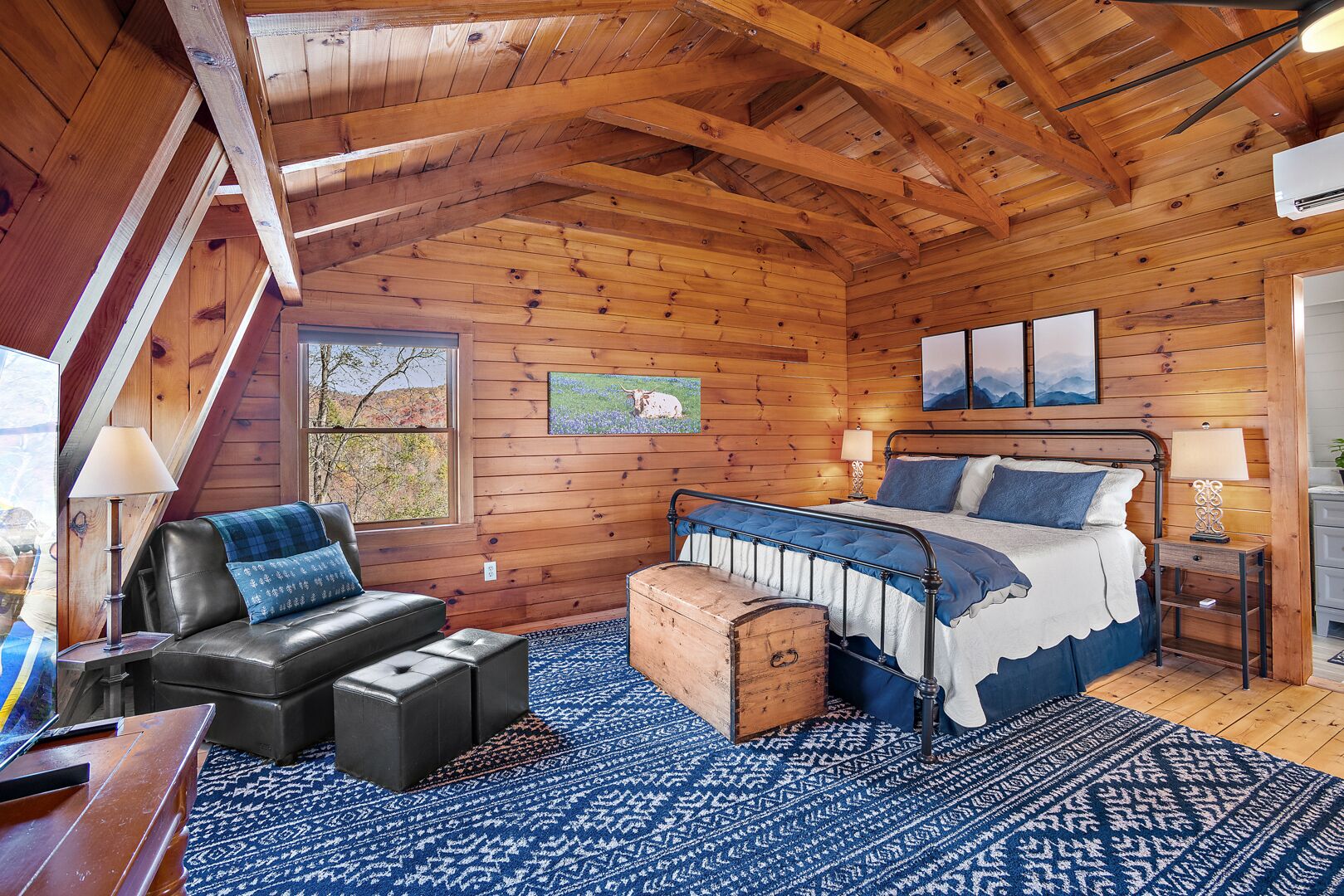 Ein Schlafzimmer in einer Blockhütte mit einem Bett, einer Ledersofa, einer Kommode und einem großen Fenster.