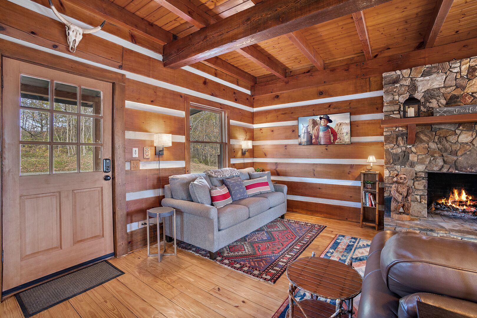 A log cabin interior with a stone fireplace, wooden beams, a sofa, and a rug.