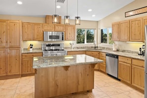 Una cocina moderna con armarios de madera, encimeras de granito, electrodomésticos de acero inoxidable e iluminación colgante.