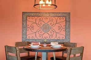 Una mesa de comedor con platos y una vela, rodeada de sillas, y un adorno decorativo en la pared superior.