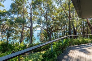 Une terrasse en bois surplombant une zone côtière, avec de grands arbres et une vue sur la mer.