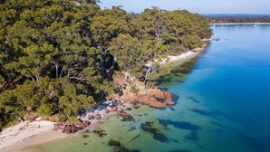 An aerial view of a coastal area with dense green trees, clear blue waters, and rocky outcrops along the shoreline. - Orion Sands: Absolute beachfront with private steps to beach (Vincentia)