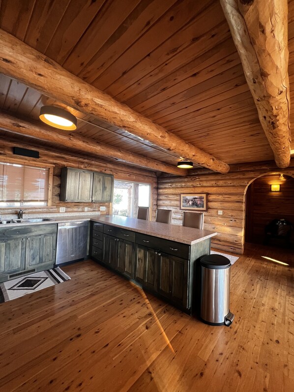 A log cabin interior with a kitchen area featuring wooden cabinets, a countertop, and a stainless steel trash can. - Spacious cabin accessing all of Colorado's outdoor adventure (Hotchkiss)