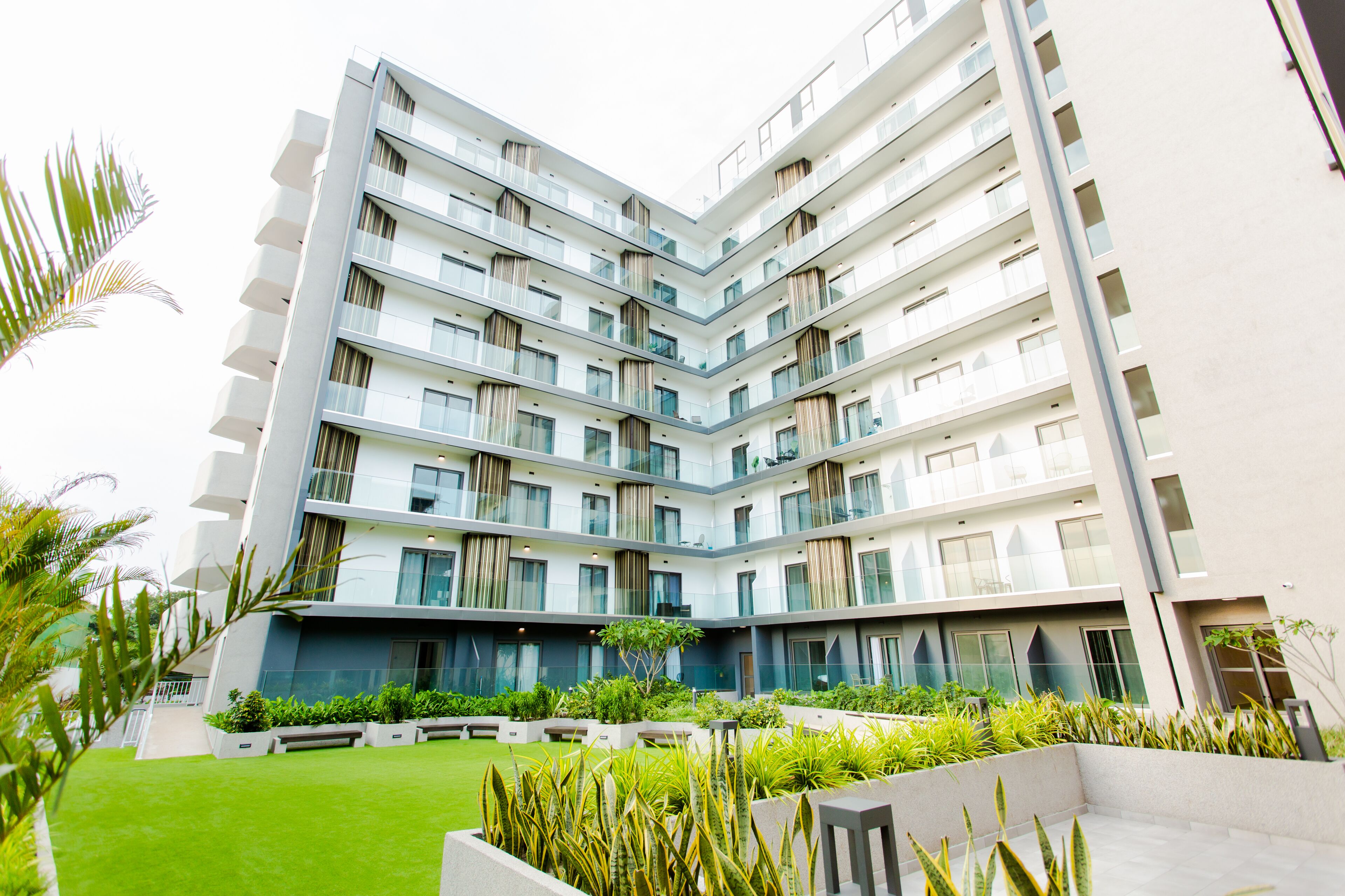A modern multi-story building with balconies, a central courtyard, and surrounding greenery.