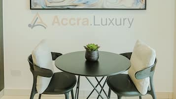 A modern dining area with a round table, two chairs, a potted plant, and a large abstract painting on the wall.