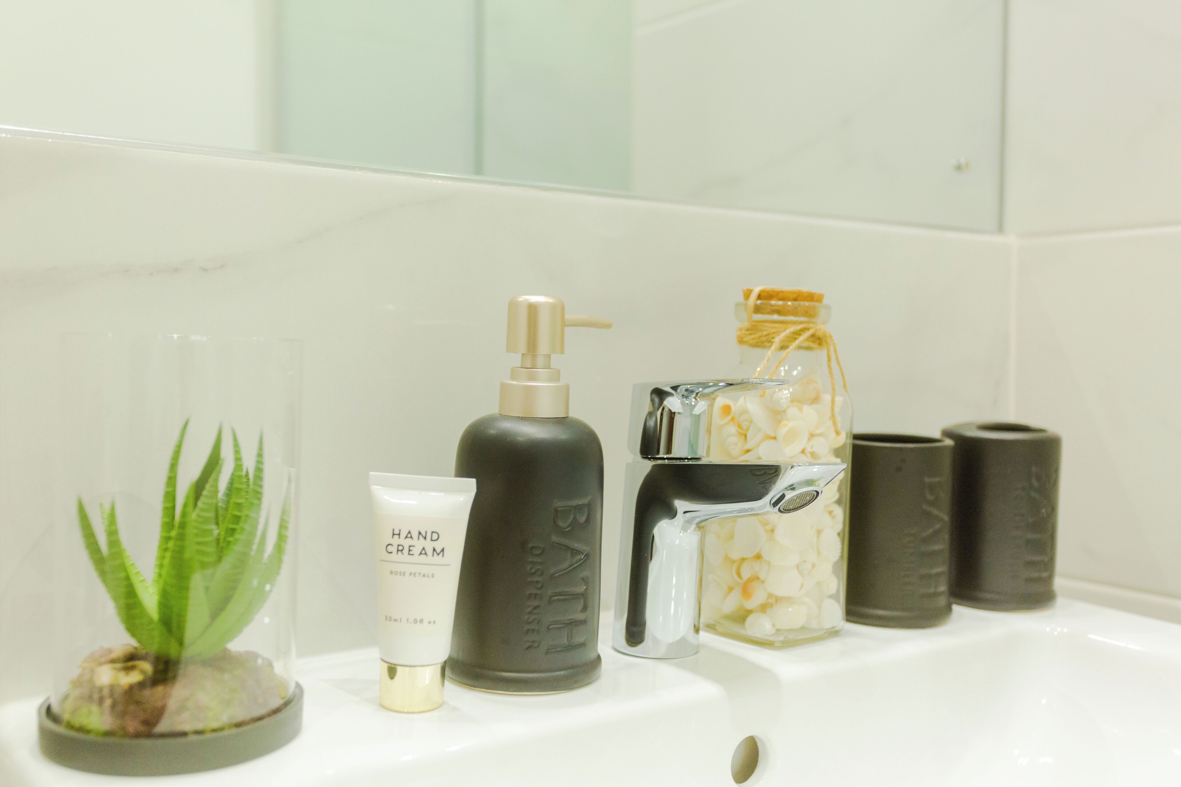 Un lavabo de salle de bain avec un distributeur de crème pour les mains, un distributeur d’huile de bain et un bocal en verre contenant des fleurs blanches.