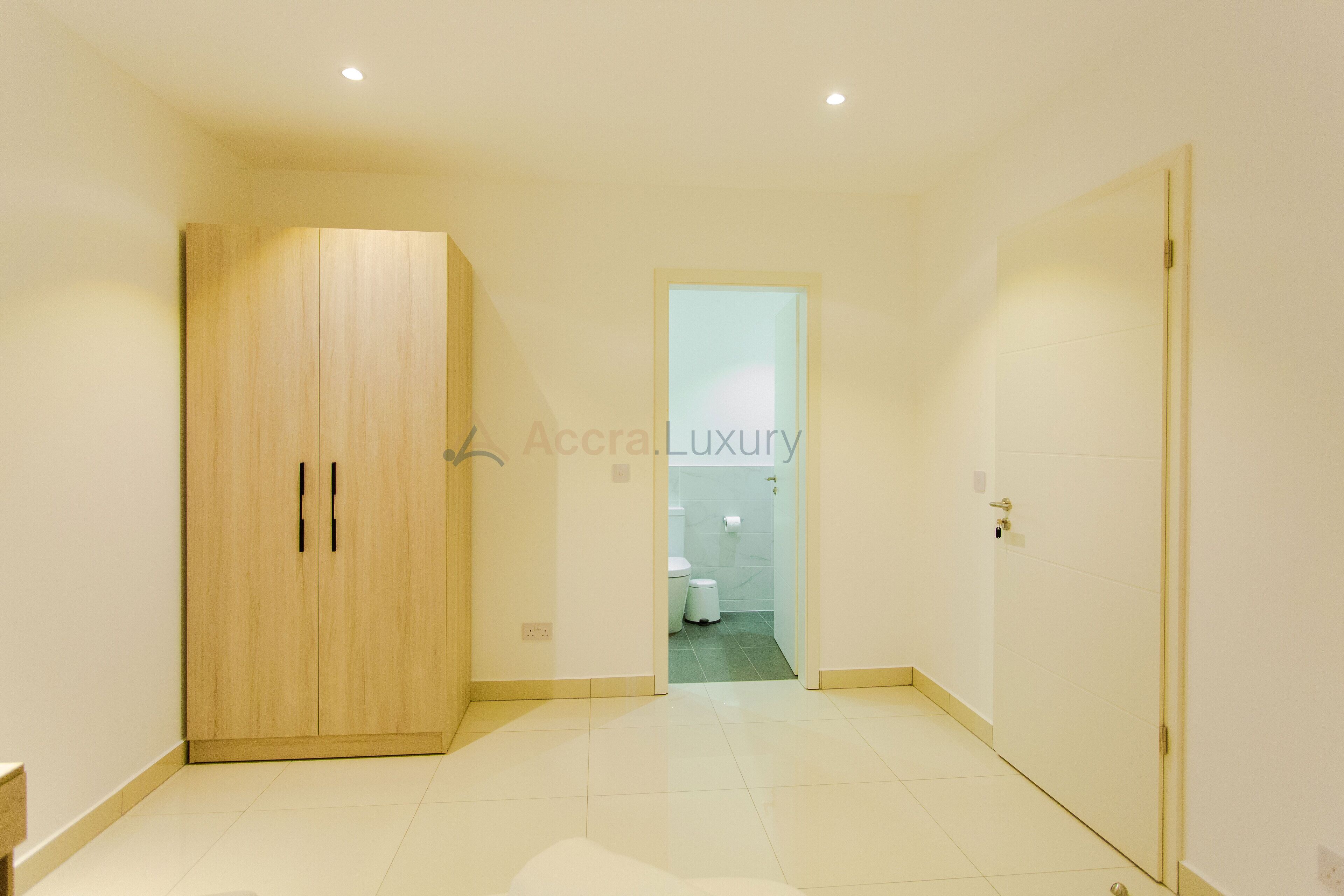 A spacious room with a large wardrobe, a door leading to a bathroom, and a tiled floor.
