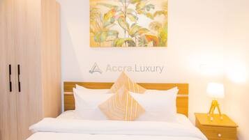 A hotel room with a bed, a nightstand, a lamp, a wardrobe, and a tropical-themed painting on the wall.