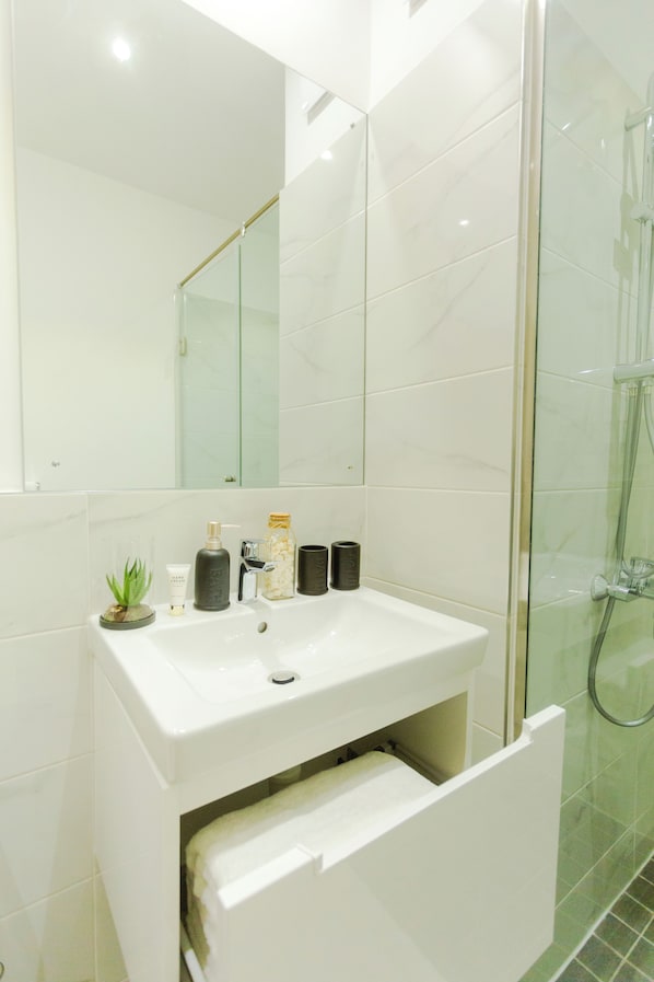Un baño moderno con lavamanos blanco, cabina de ducha de vidrio y espejo sobre el lavamanos.