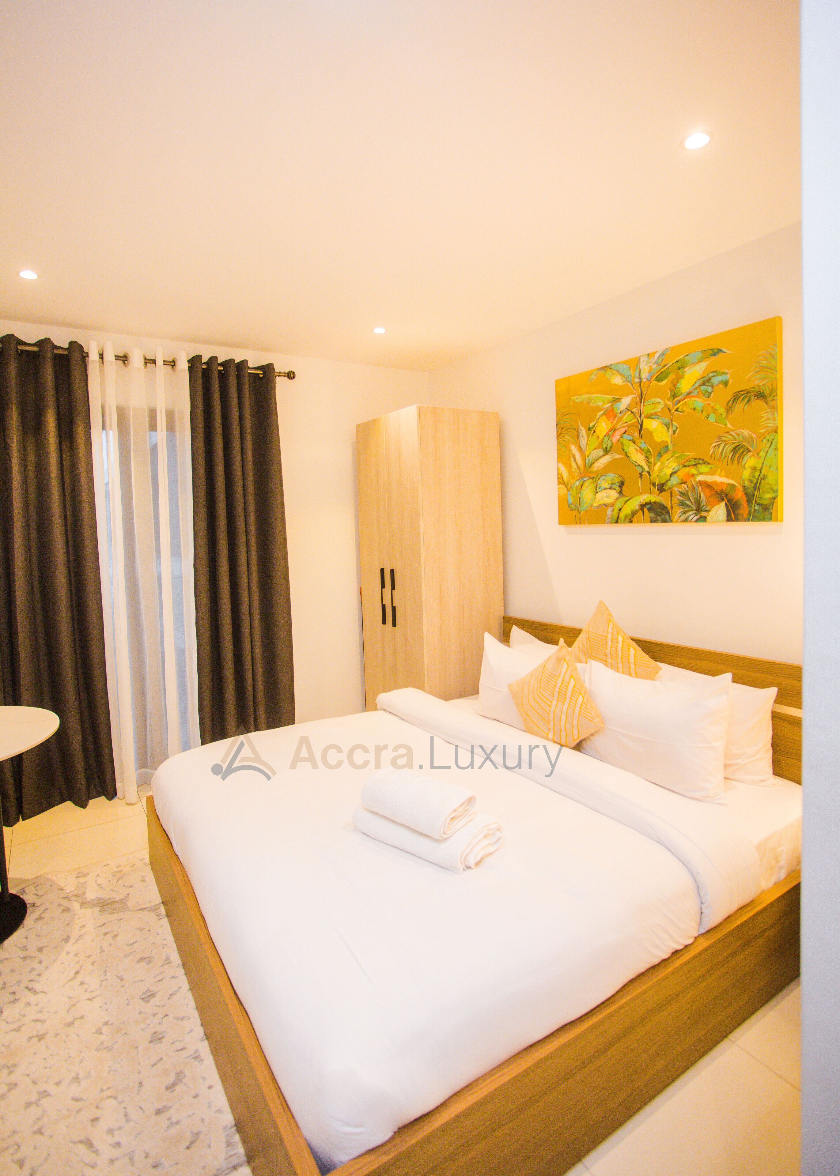 A hotel room with a bed, a wardrobe, a painting on the wall, and a window with curtains.