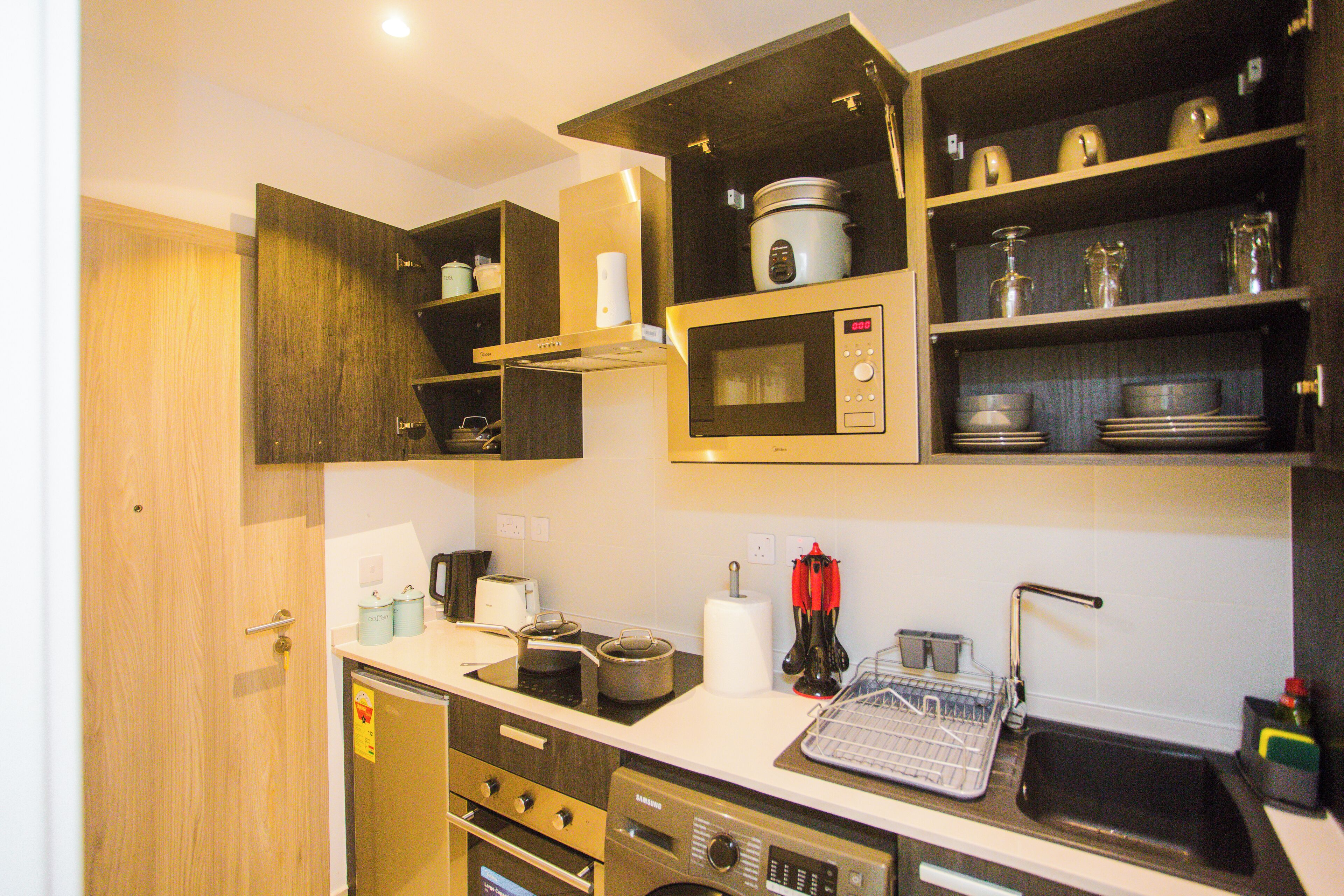 A compact kitchen with built-in appliances, wooden cabinets, and a dish drying rack.