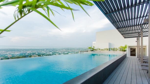 A rooftop infinity pool with a city view, wooden deck, and a covered seating area.