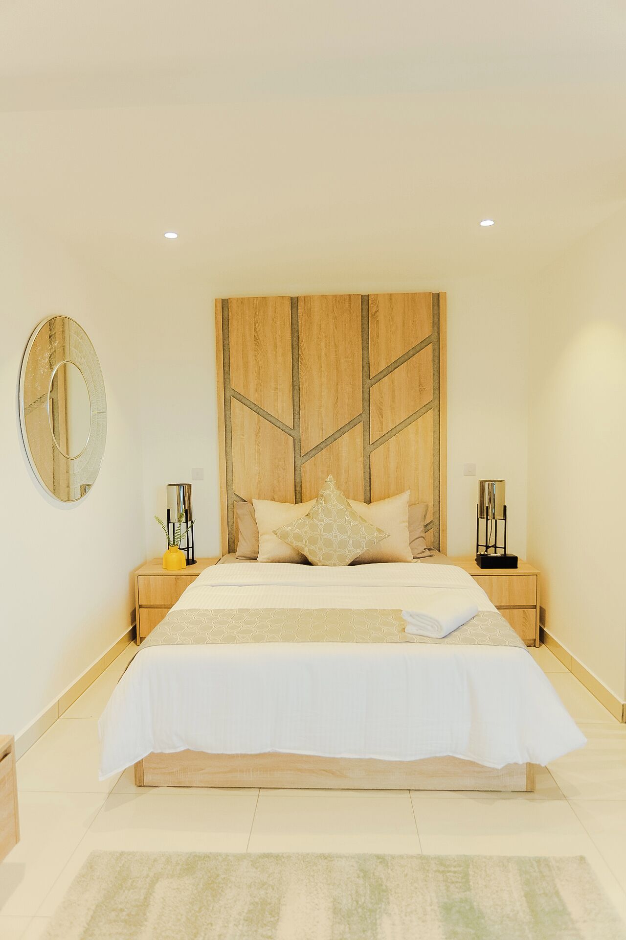 Un dormitorio moderno con una cama grande, cabecero de madera, mesitas de noche y un espejo.