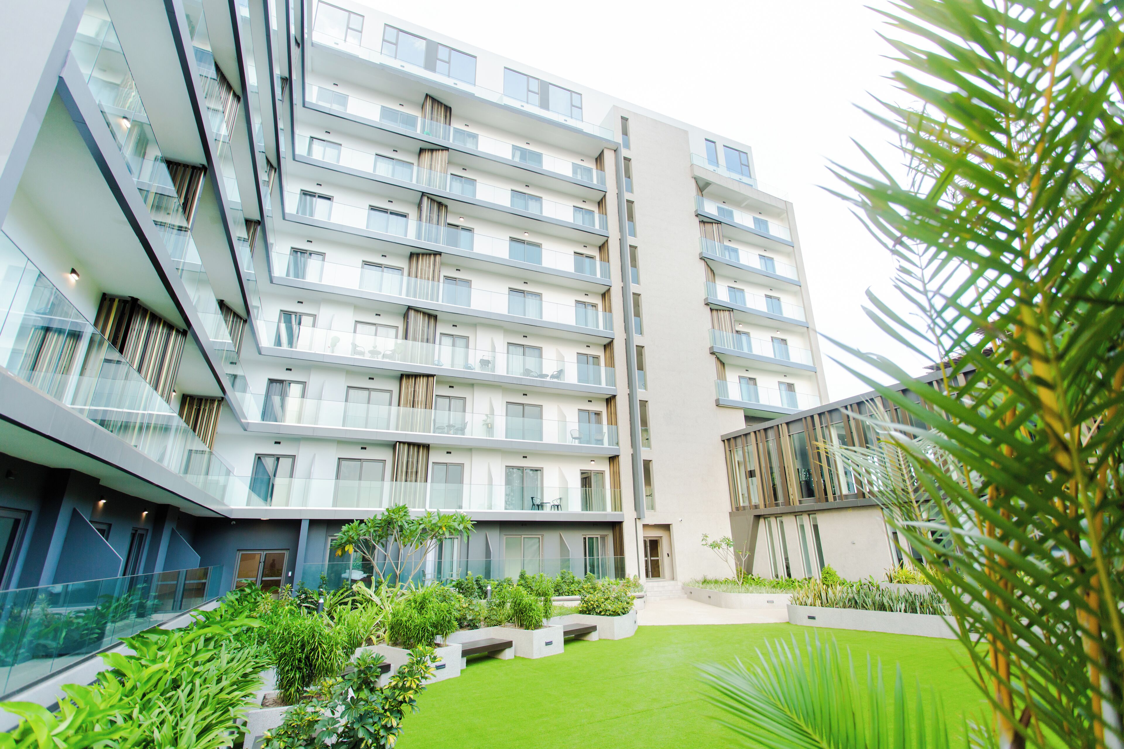 A modern multi-story building with balconies, a central courtyard with greenery, and a mix of glass and concrete architecture.