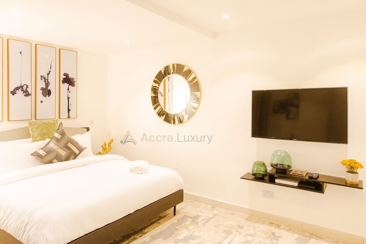 Une chambre à coucher moderne avec un grand lit, un téléviseur à écran plat fixé au mur et un miroir décoratif placé au-dessus.