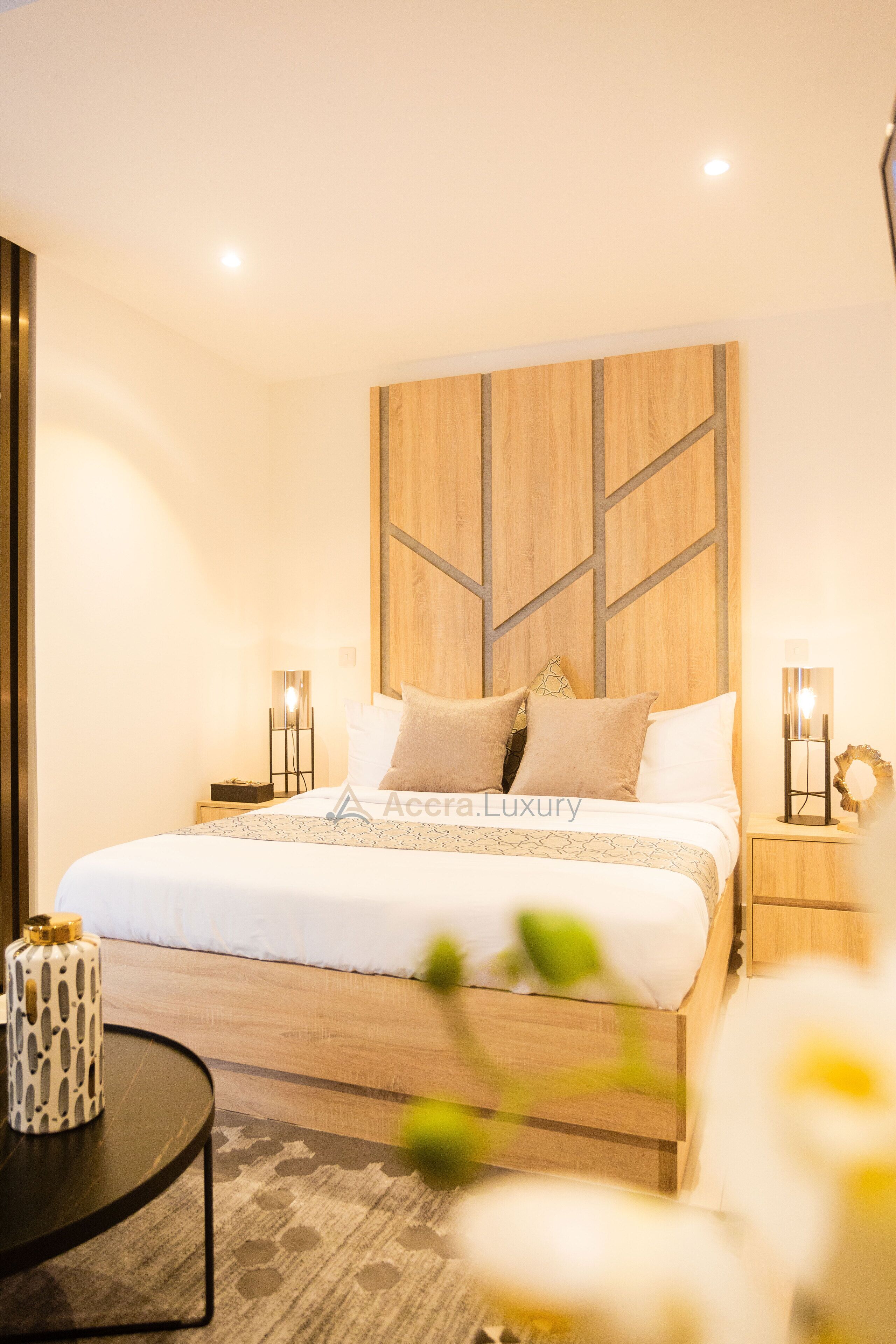 Un dormitorio moderno con cabecera de madera, cama bien hecha, lámparas de noche y una mesita con un objeto decorativo.