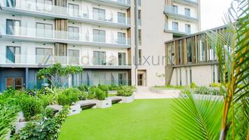 Un immeuble moderne à plusieurs étages, doté de balcons, d’une cour intérieure avec une pelouse artificielle et d’une variété de plantes.