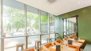 A restaurant with wooden tables and chairs, large windows, and a view of the street outside.