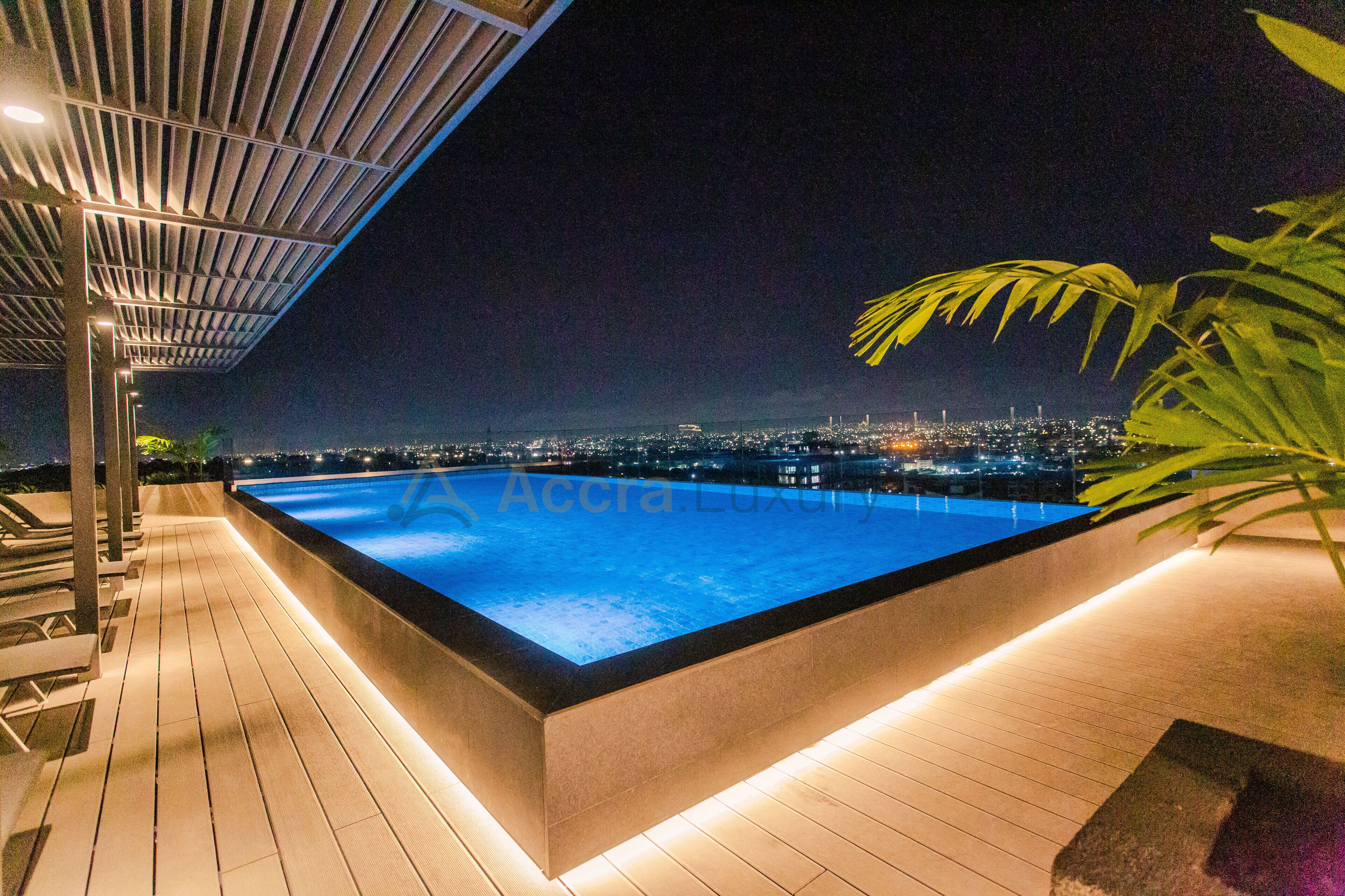 A nighttime view of a rooftop pool with a cityscape in the background.