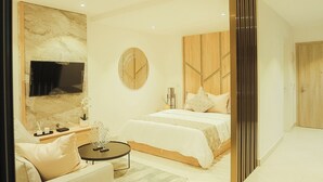 A modern hotel room with a large bed, a sofa, a TV, and a decorative wall.