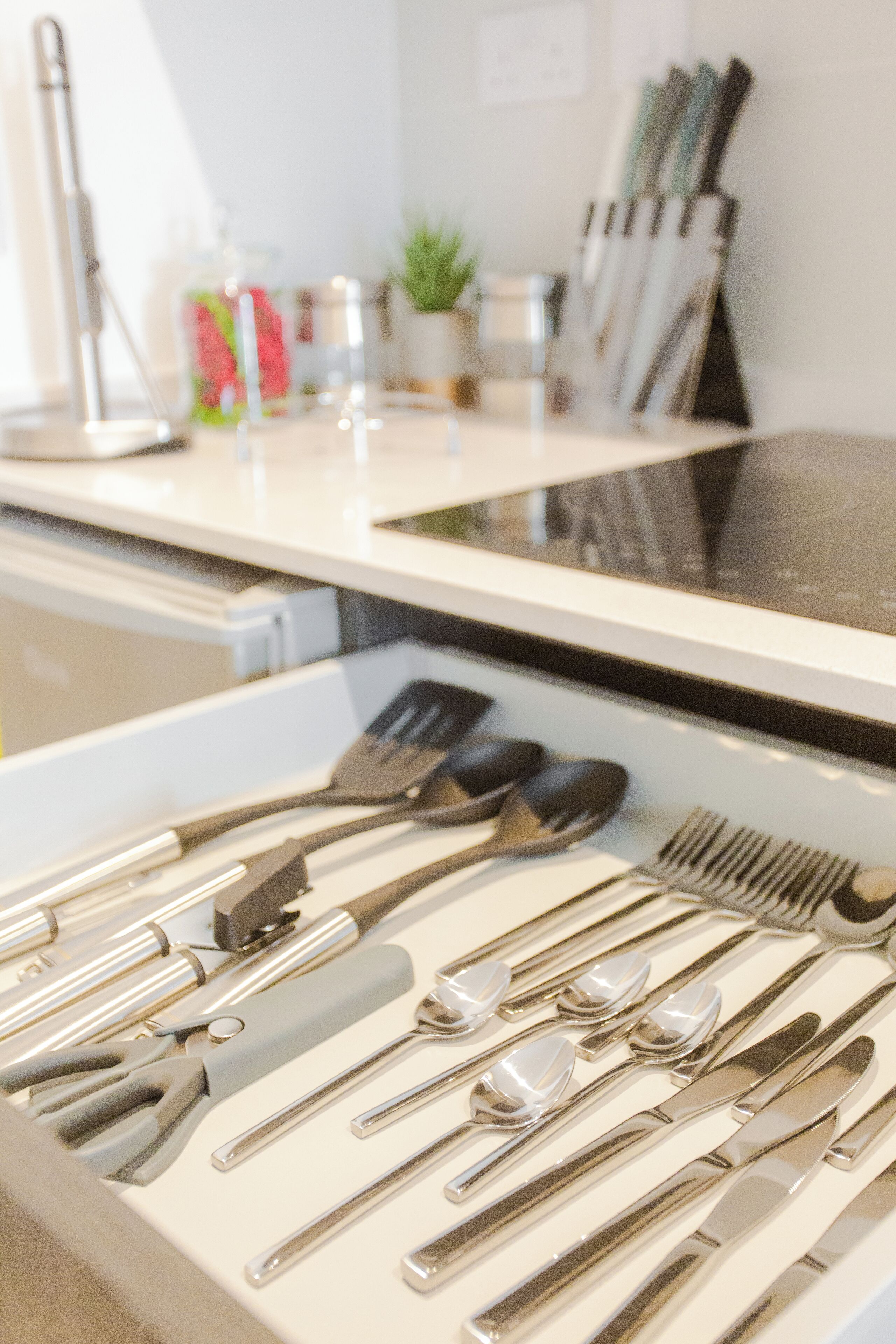 A neatly arranged set of silverware on a white tray, including forks, spoons, and knives.