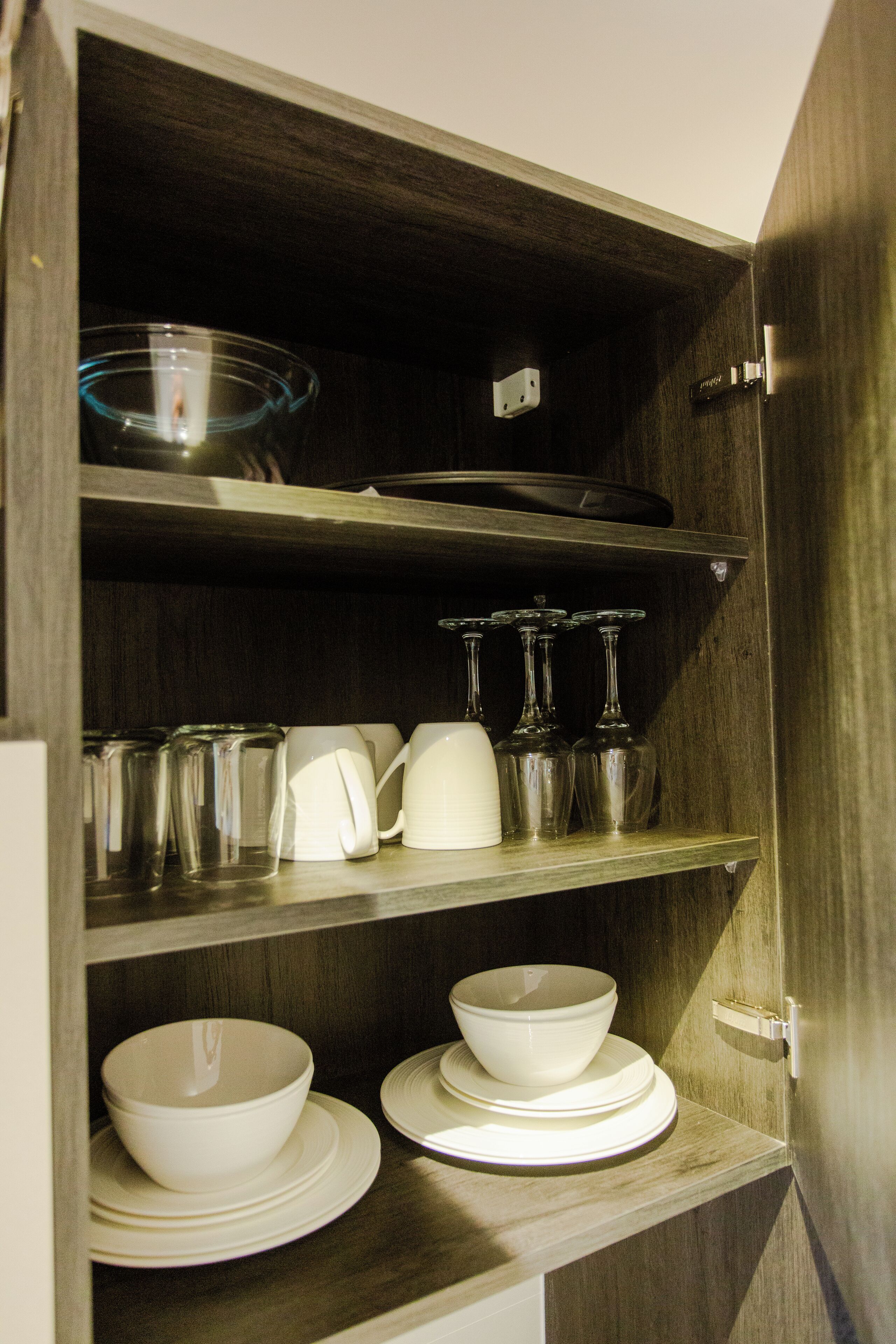 A wooden cabinet with shelves containing bowls, plates, glasses, and a coffee pot.