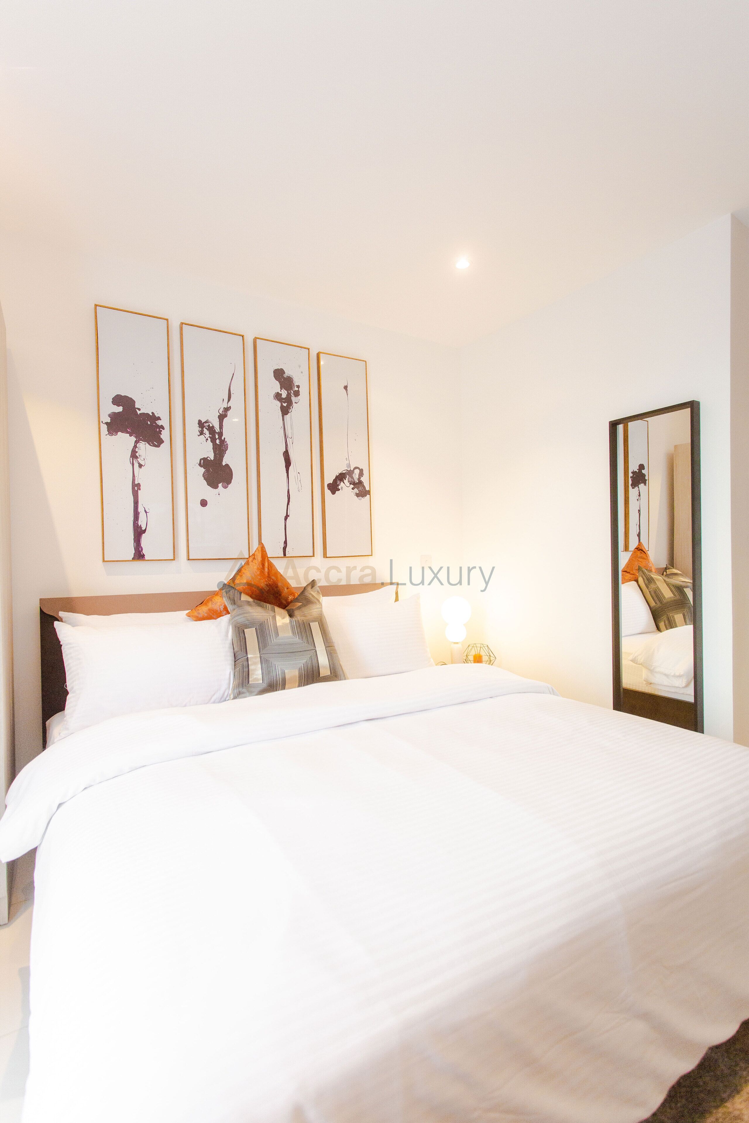 A hotel room with a large bed, a nightstand, a mirror, and three framed artworks on the wall.