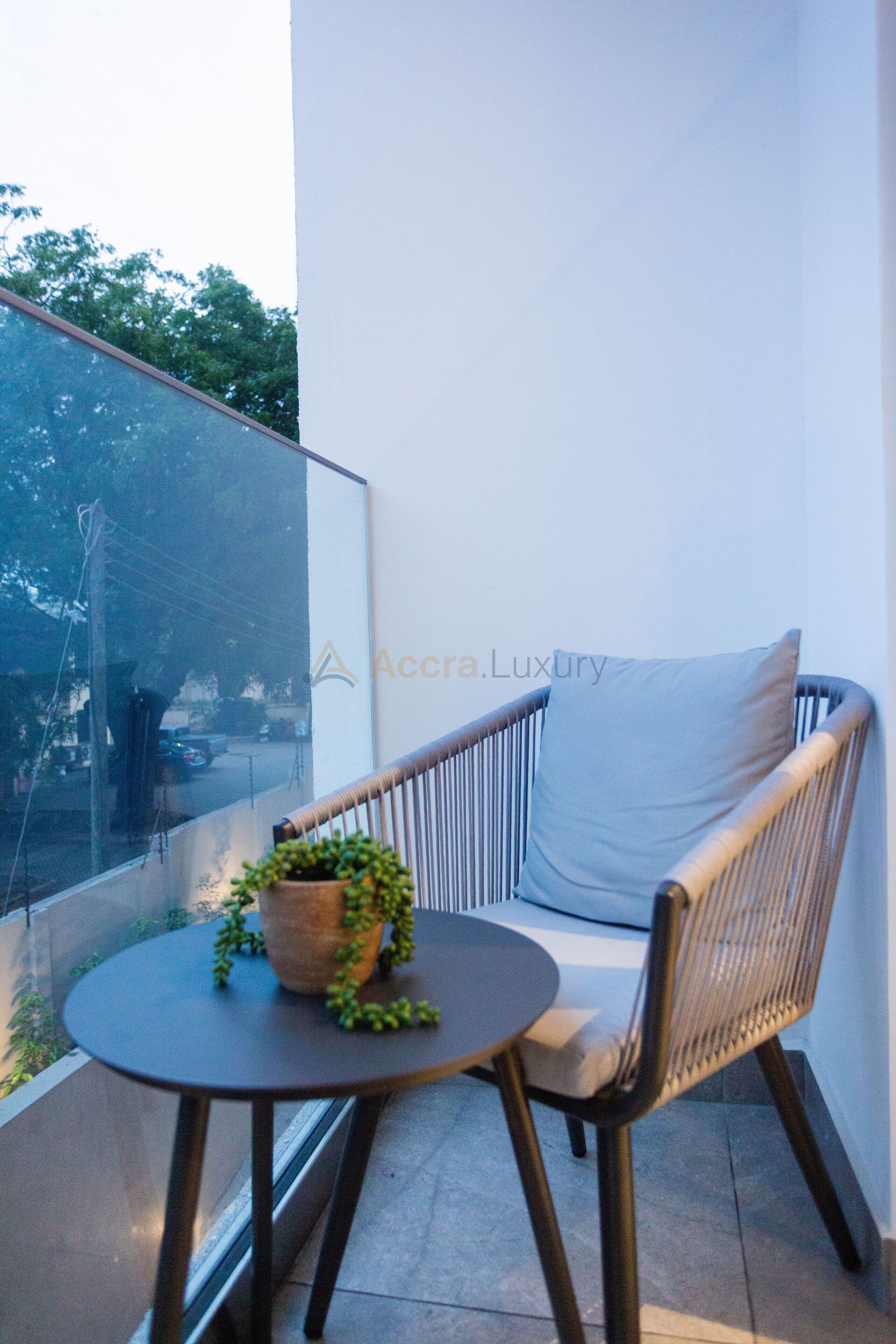 A balcony with a wicker chair, a small round table, and a potted plant.