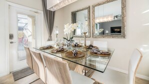A dining area with a glass table, white chairs, and a chandelier. There are two mirrors on the wall and a vase with flowers. - "Sweet Retreat" - Free Pool Heat & Bbq (Kissimmee)