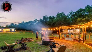 An outdoor area with a fire pit, seating, and a covered structure with string lights.