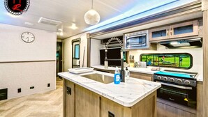 A modern kitchen with a central island, built-in oven, and a television mounted above the counter.