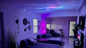 A modern living room with a sectional sofa, a flat-screen TV, and a ceiling with a galaxy light display.