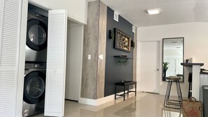 A modern laundry room with stacked washers and dryers, a wooden accent wall, a mirror, and a small seating area.