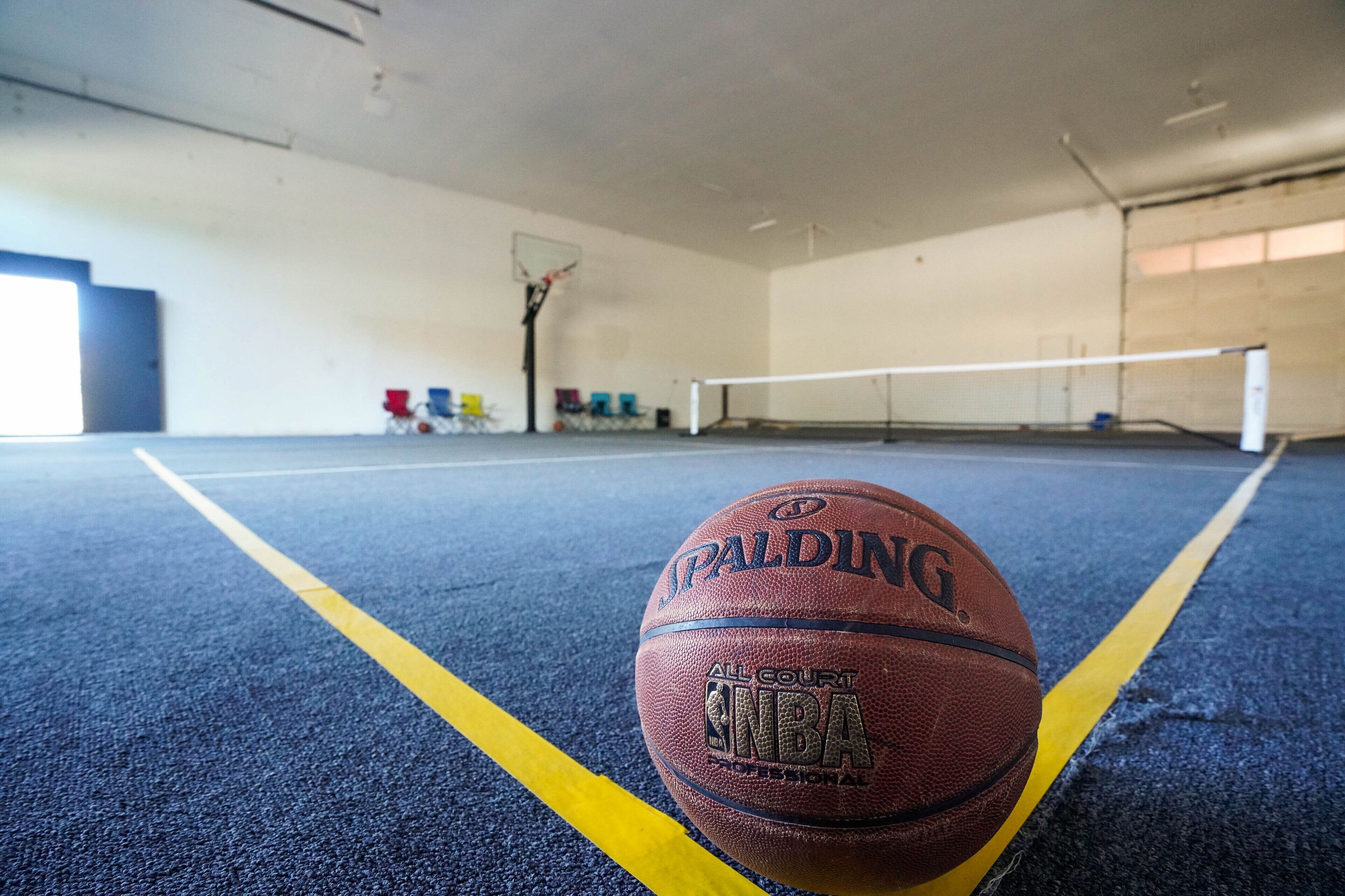 A basketball on an indoor court with a net and a basketball hoop.