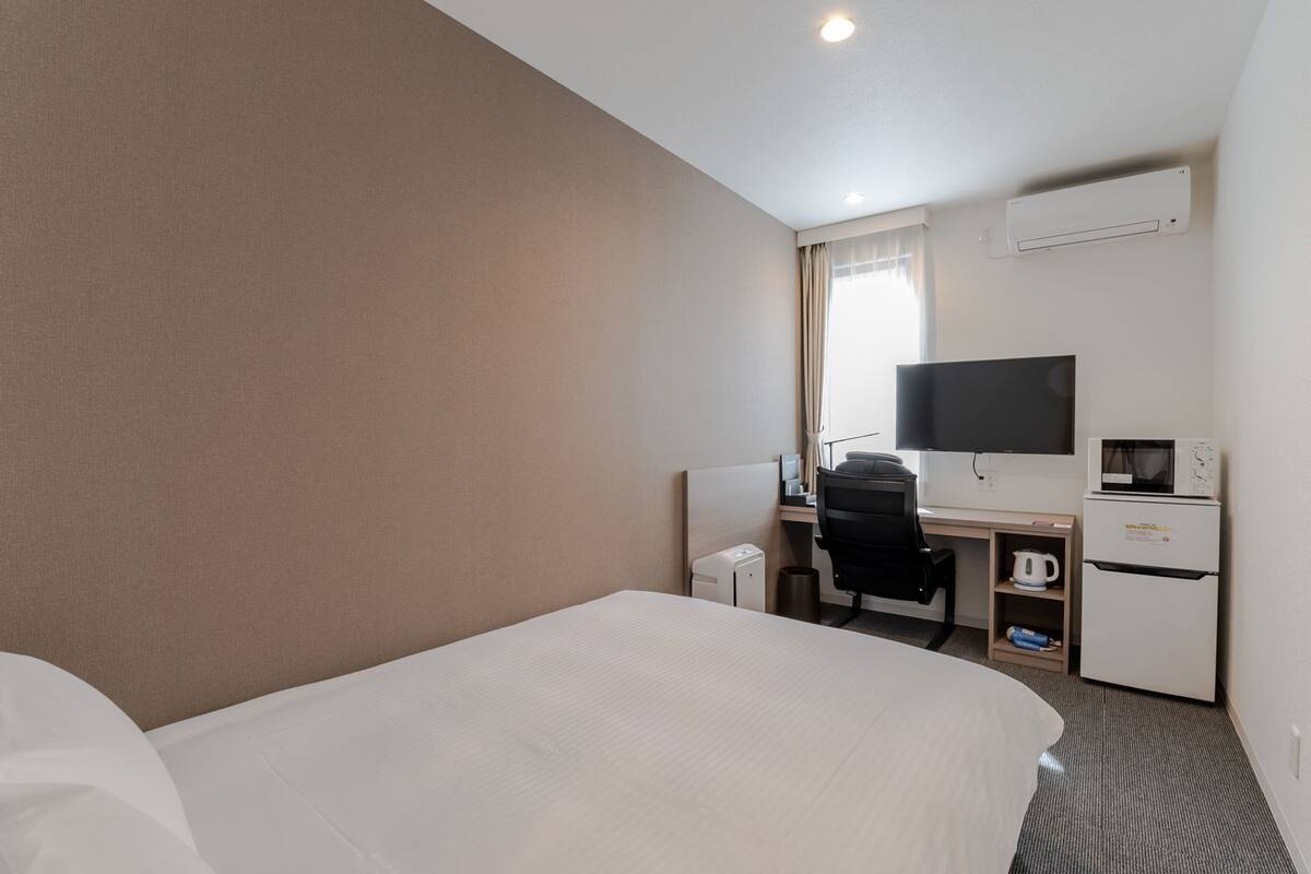 A hotel room with a bed, desk, chair, TV, microwave, and small refrigerator.