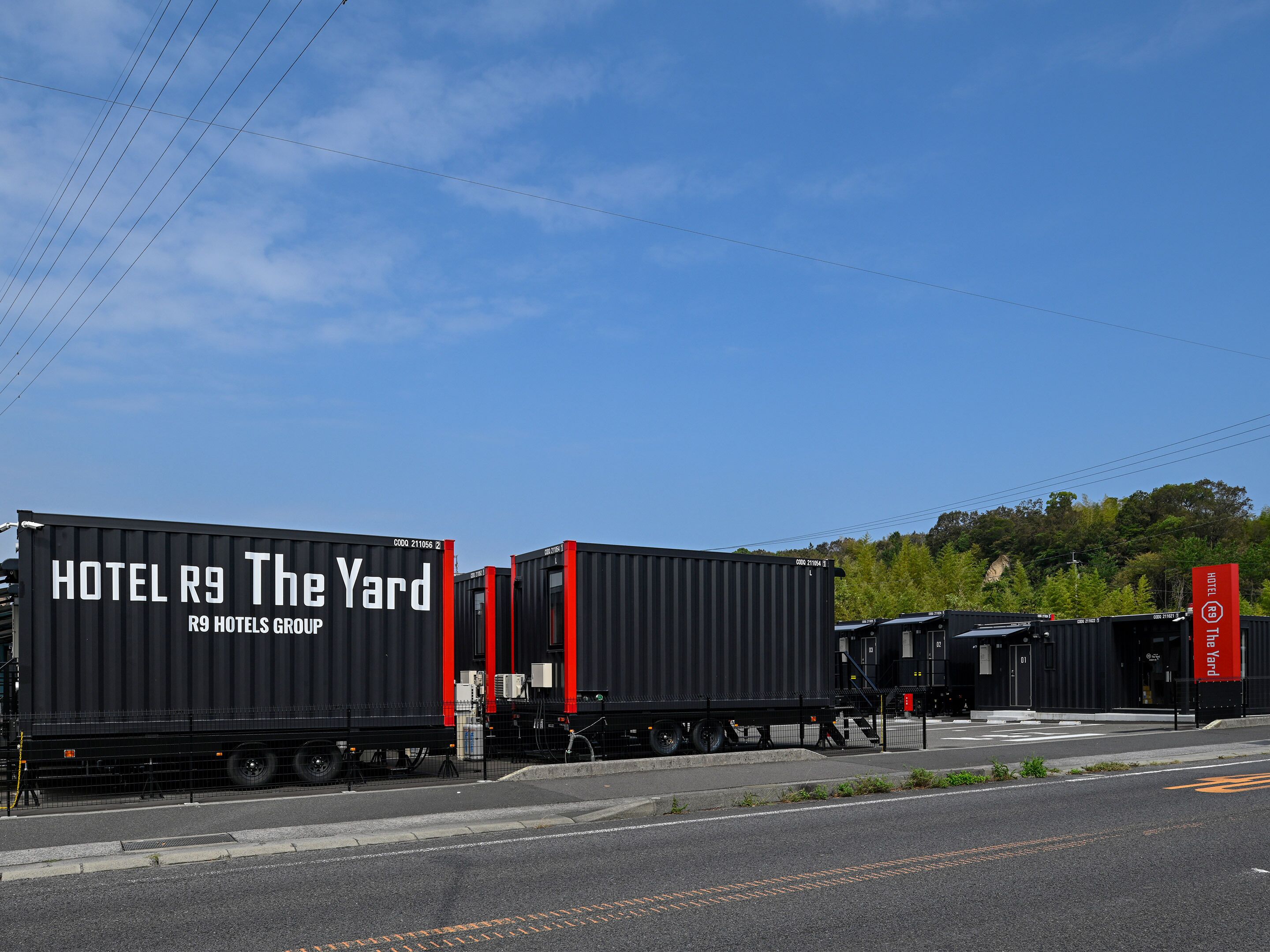 A series of black shipping containers with red accents, labeled as HOTEL R9 The Yard, part of the R9 Hotels Group.