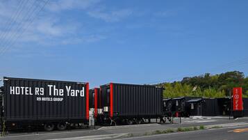 A series of black shipping containers with red accents, labeled as HOTEL R9 The Yard, part of the R9 Hotels Group.