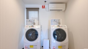 Two front-loading washing machines in a narrow hallway with wooden flooring and white walls. - HOTEL R9 The Yard Shikokuchuo (Shikokuchuo)