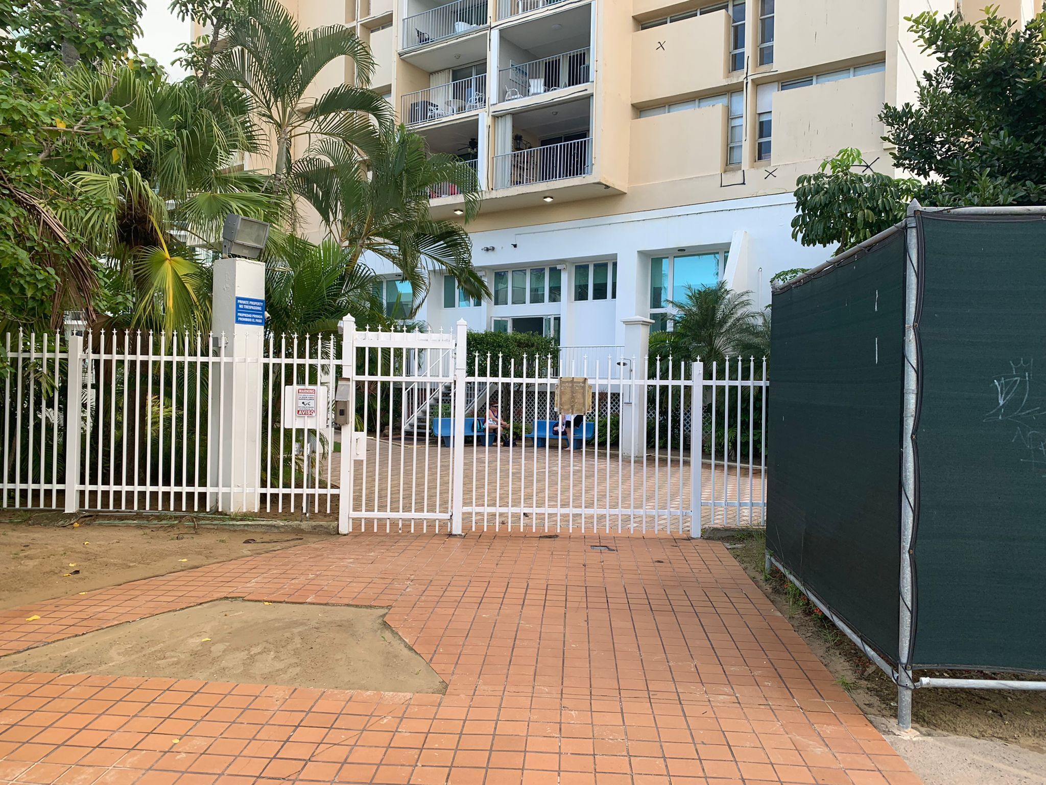 A gated entrance to a residential building with a paved driveway and a fenced area.
