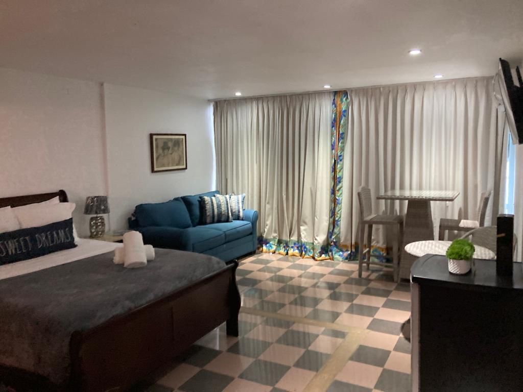 Quarto de hotel com uma cama, um sofá azul, uma escrivaninha e um chão xadrez.