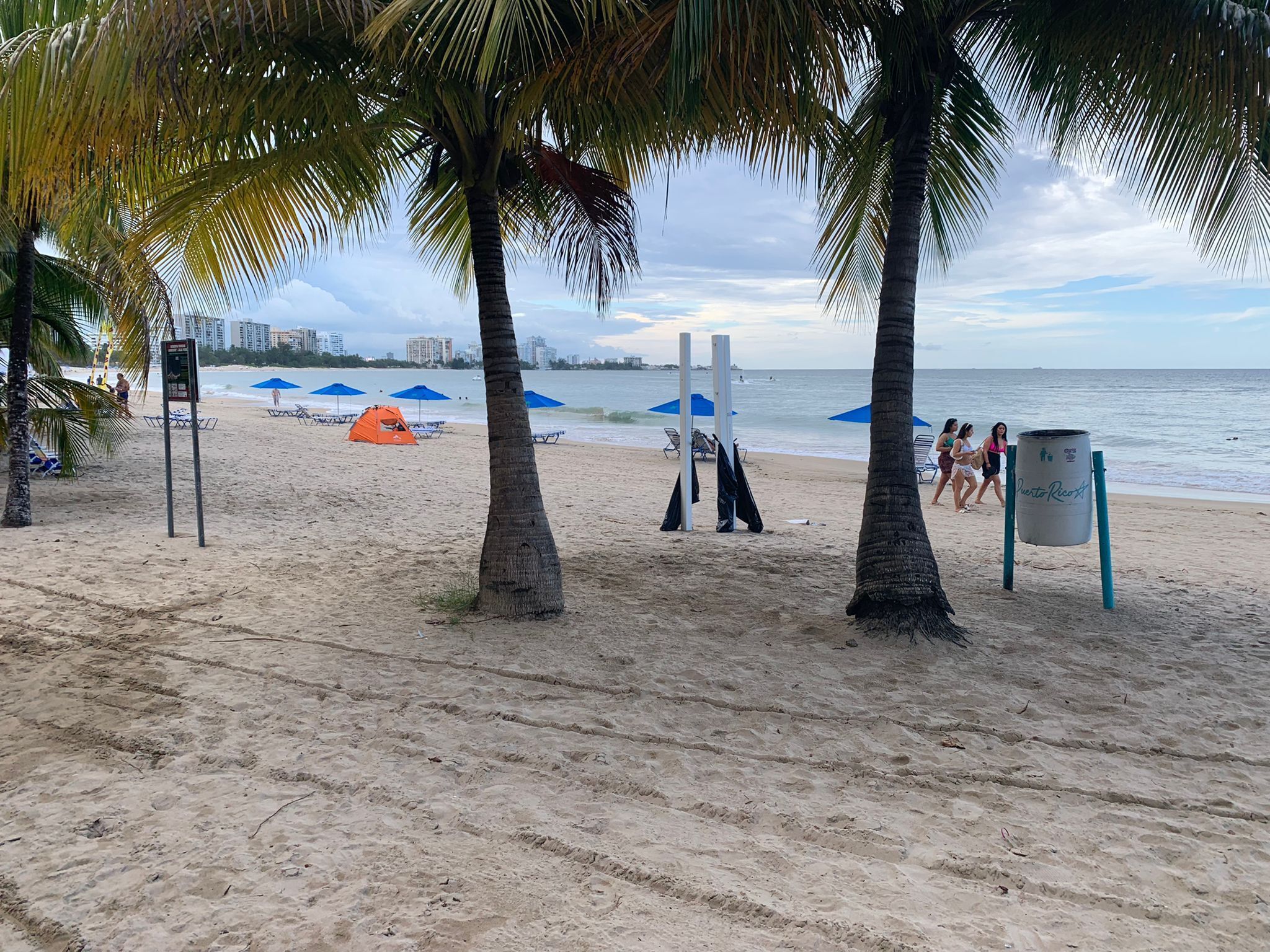 Une plage bordée de palmiers, avec des tentes et des parasols.