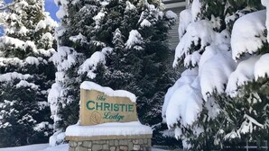 A snow-covered sign for The Christie Lodge with a stone base, surrounded by snow-laden trees. - Christie Lodge Avon Vail for New Years (Avon)