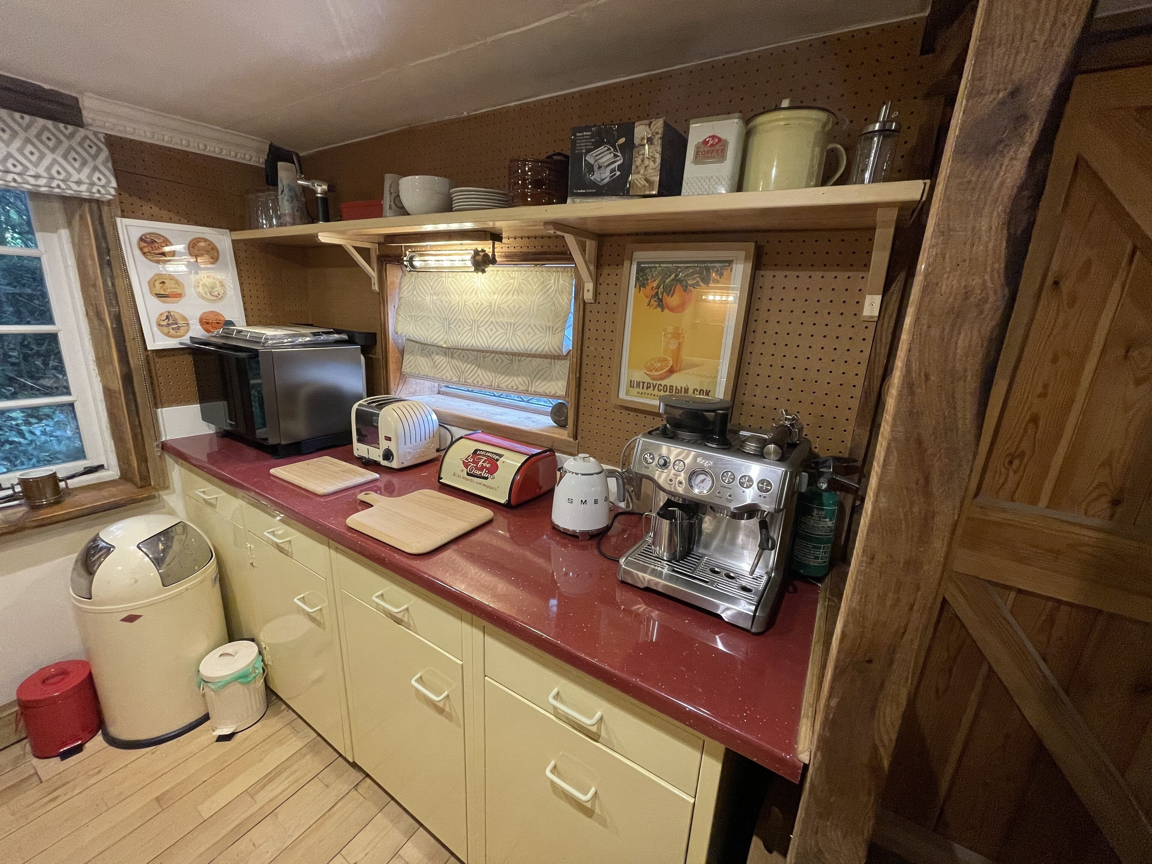 Une cuisine avec un plan de travail rouge, une machine  à café, un grille-pain et une cuisinière. Il y a des placards sous le plan de travail et une fenêtre au-dessus.