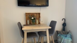 Un coin repas avec une table en bois, deux chaises, un vase de fleurs et un téléviseur fixé au mur.